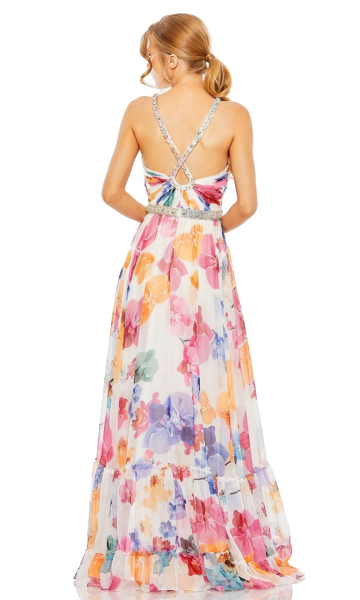 A woman stands facing away, wearing the Long Formal Dress 2219 by Mac Duggal—a sleeveless, floor-length floral A-line gown featuring crisscross straps and a beaded belt.